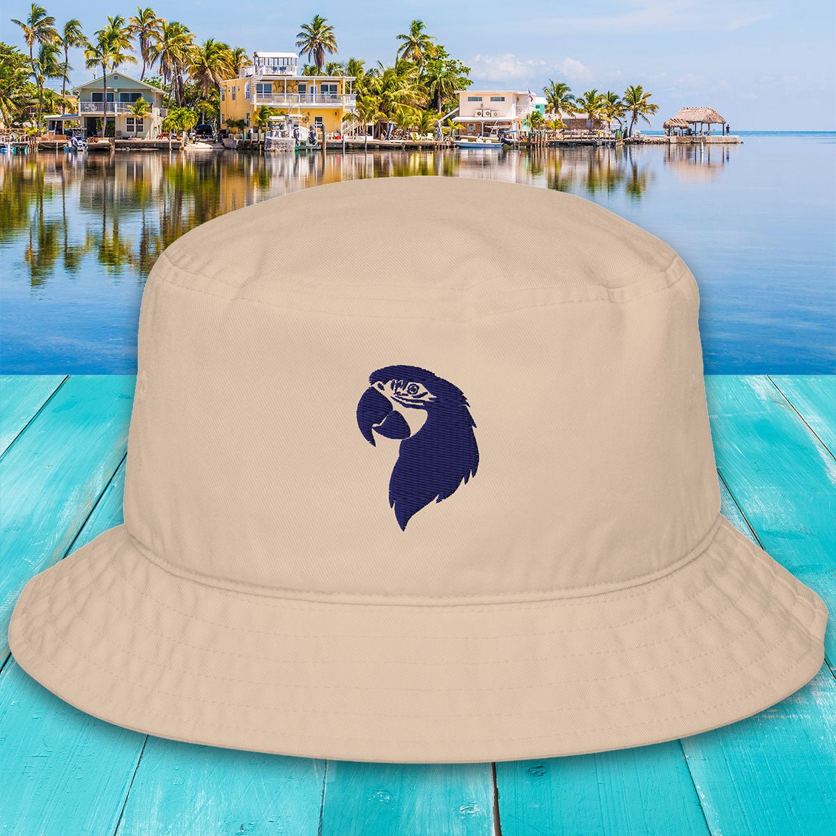 Beige bucket hat with a blue parrot design on a turquoise wooden surface with a tropical background.