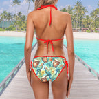Woman wearing a colorful bikini with a tropical pattern on a wooden pier with turquoise water and palm trees in the background.