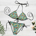 Tropical-themed bikini set with floral and parrot design on a white nautical wood background.