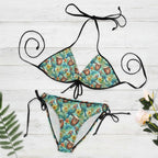 Tropical-themed bikini set with floral and parrot design on a white nautical wood background.