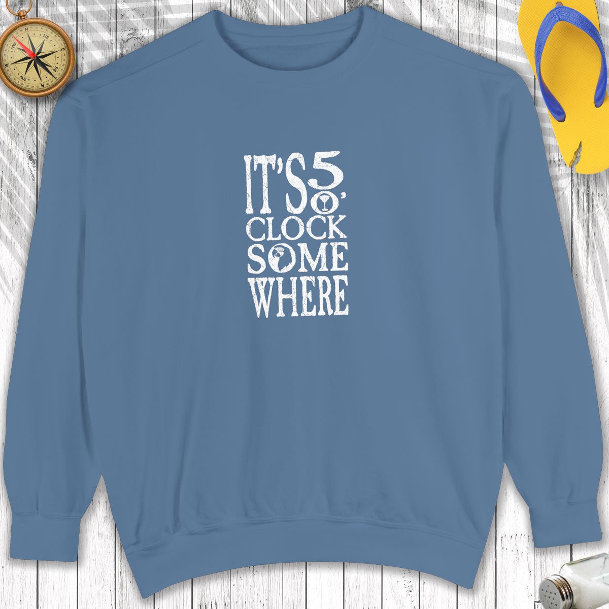 Blue sweatshirt with 'It's 5 o'clock somewhere' text on a wooden surface.