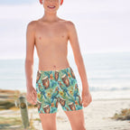 Boy wearing colorful swim shorts with a tropical ParrotHead pattern on a Hawaiian beach.