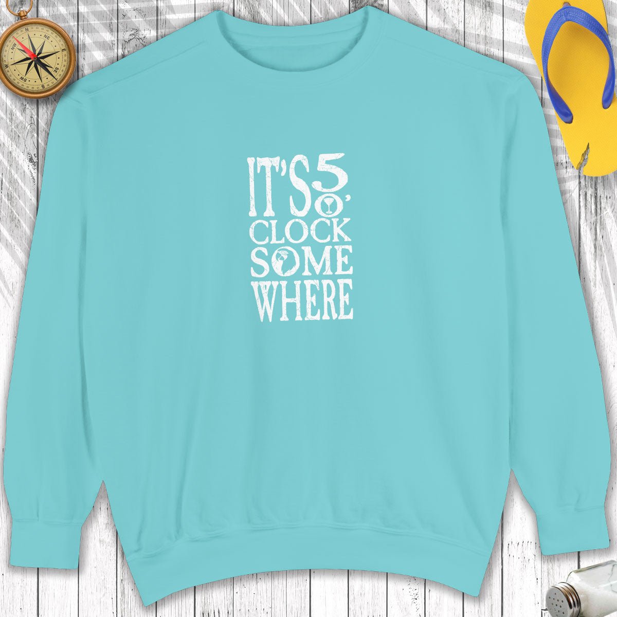 Light blue sweatshirt with 'It's 5 o'clock somewhere' text on a wooden surface.