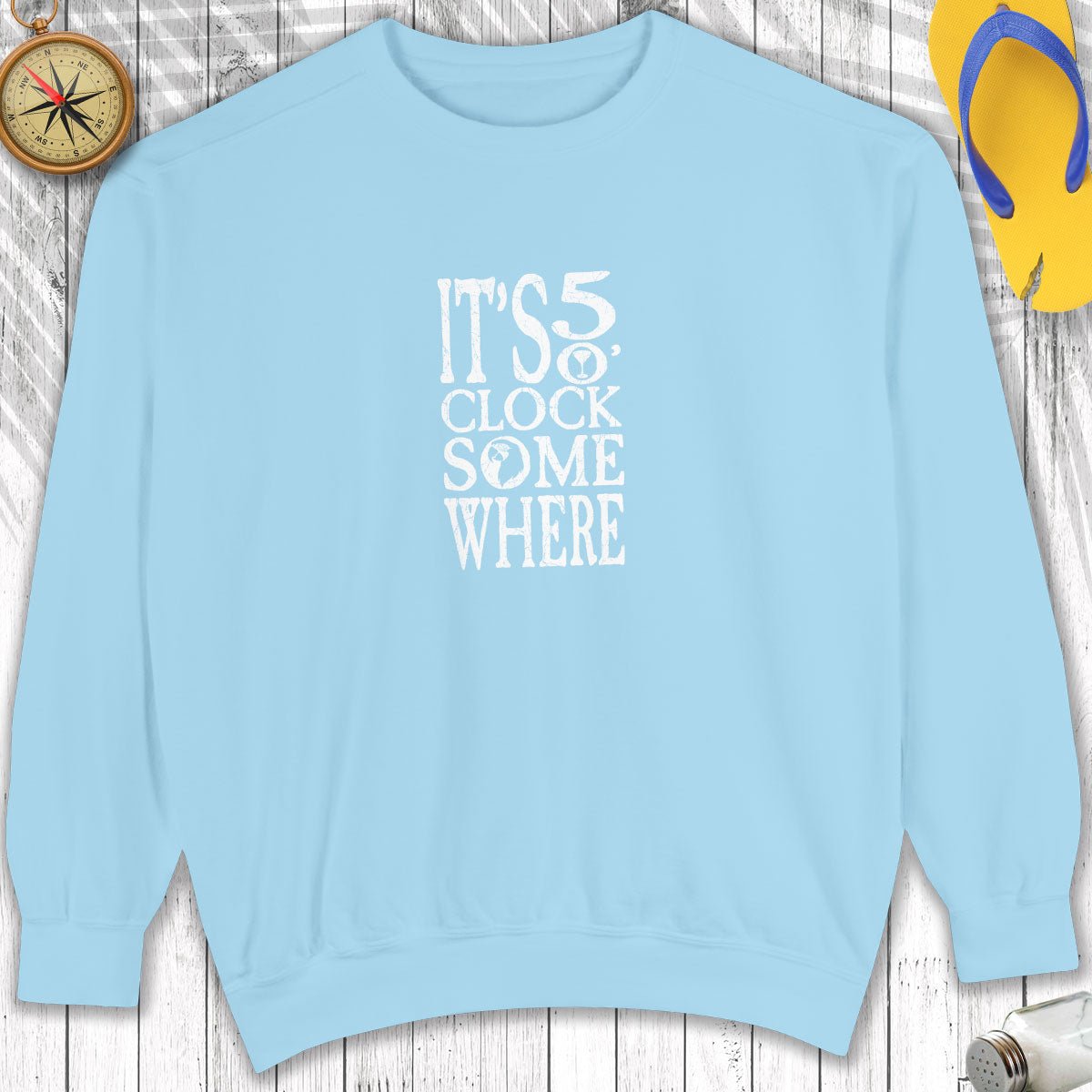 Light blue sweatshirt with 'It's 5 o'clock somewhere' text on a wooden surface.