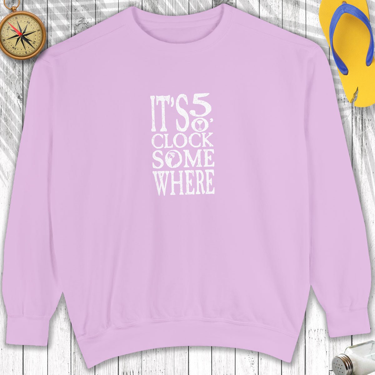 Purple sweatshirt with 'It's 5 o'clock somewhere' text on a wooden surface.