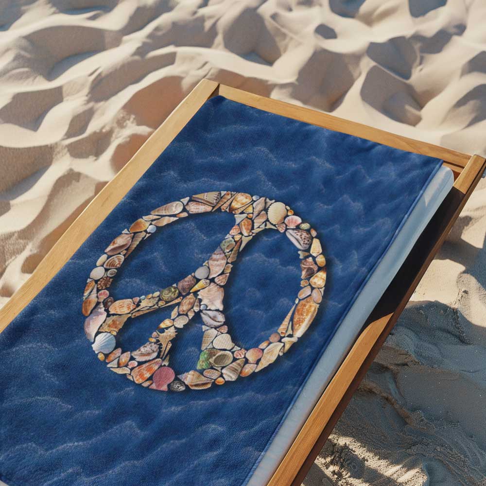 Beach towel with peace sign made out of seashells laid out flat on beach lounge chair over the sand