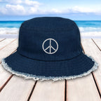 Navy blue bucket hat with peace symbol on a wooden surface with beach background