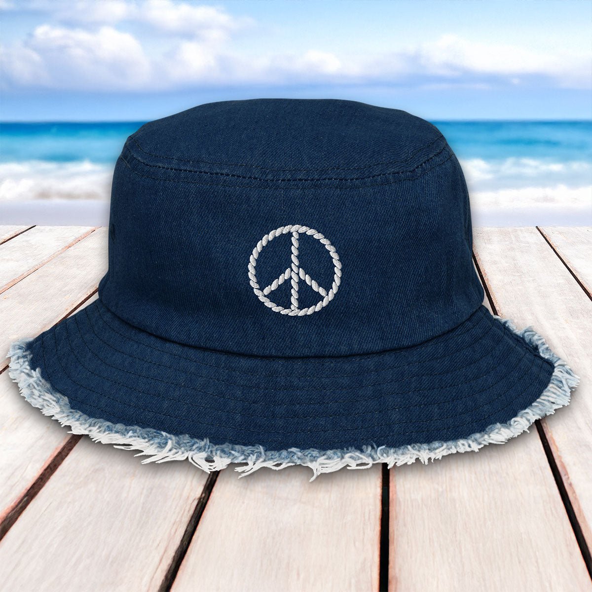Navy blue bucket hat with peace symbol on a wooden surface with beach background