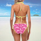 Woman wearing a yellow bikini top and pink bottom with dolphin pattern on a beach.