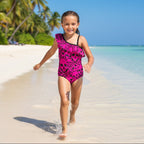 Pink Pirate swimsuit with black skull and crossbones pattern on an adventurous little girl running along the water's edge on a tropical island beach