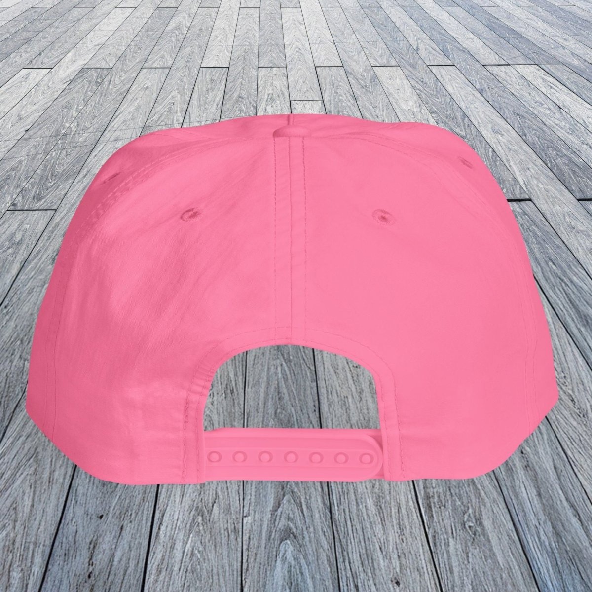 A bright pink baseball cap viewed from the back, placed on a gray wooden plank floor.
