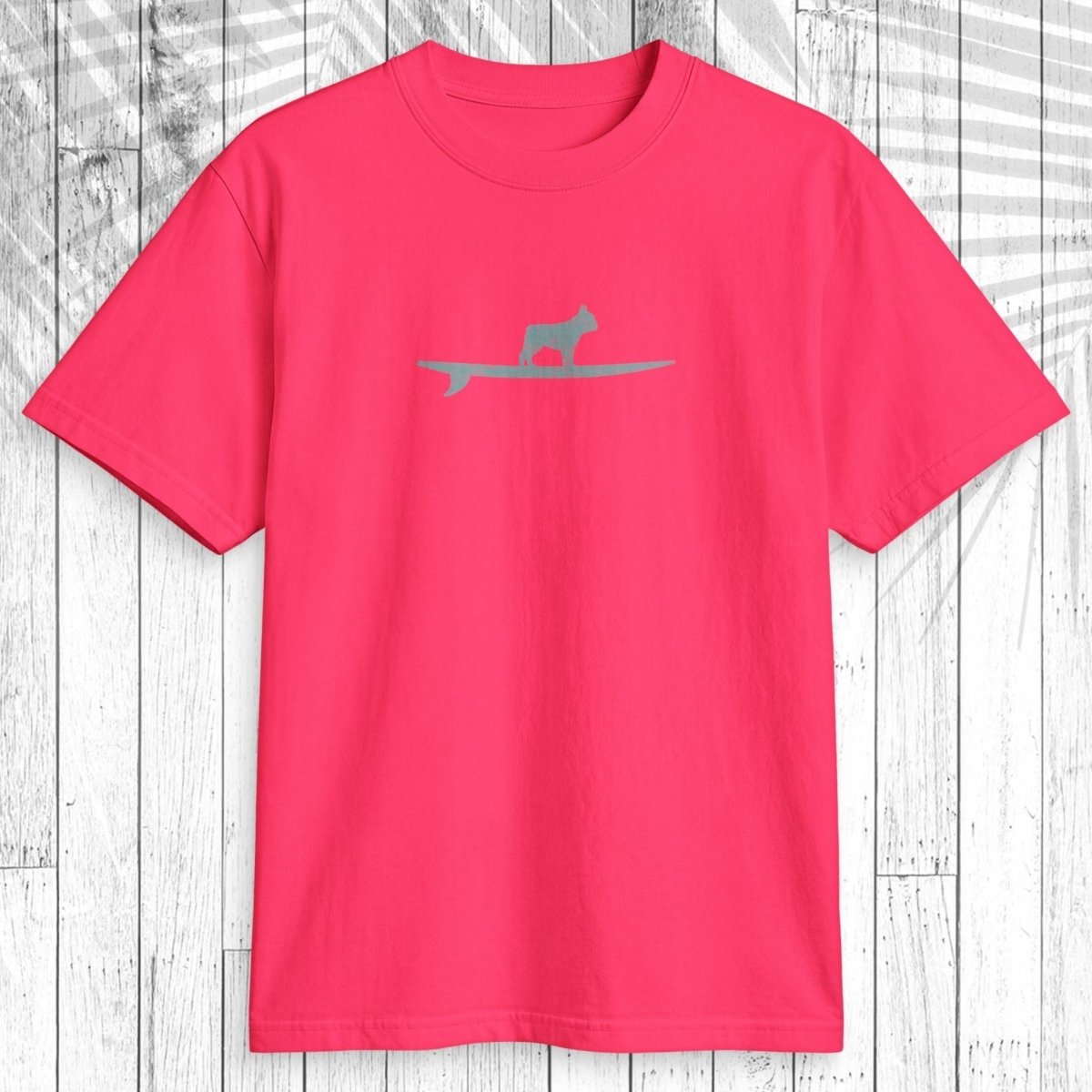 A bright pink short-sleeve t-shirt with a small gray silhouette of a cat on a surfboard across the chest, displayed flat against a white wood plank background.