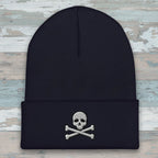 A dark navy blue ribbed knit beanie hat featuring an embroidered silver skull and crossbones on the front cuff, set against a plain white background.
