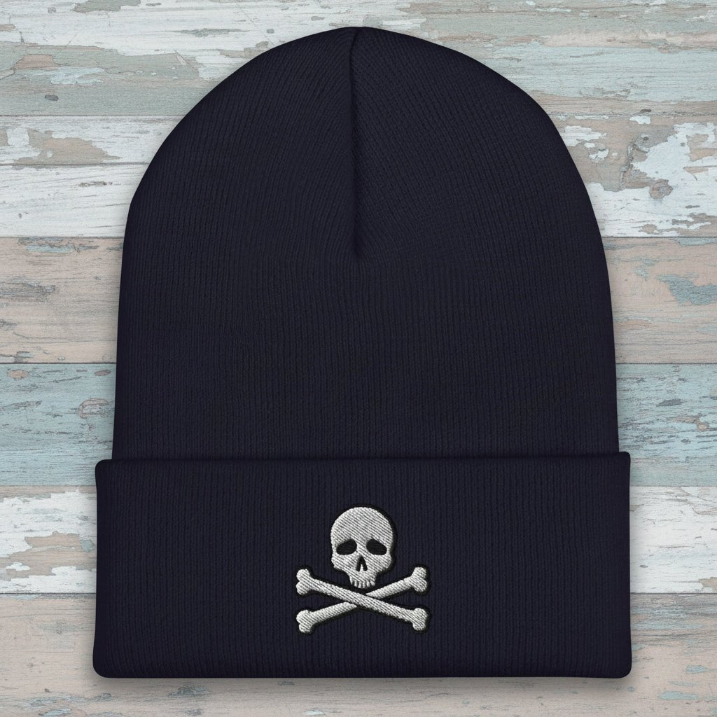 A dark navy blue ribbed knit beanie hat featuring an embroidered silver skull and crossbones on the front cuff, set against a plain white background.