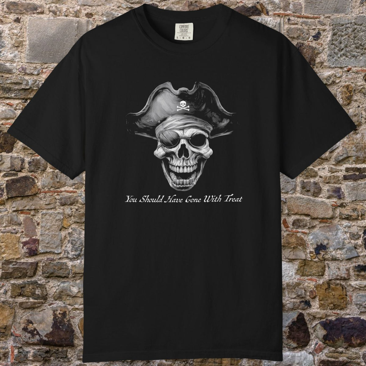 A black short-sleeve crewneck t-shirt featuring a grayscale graphic of a skull wearing a pirate hat with a skull-and-crossbones symbol, and the text 'You Should have gone with treat' below. The t-shirt is displayed flat against a rustic, textured stone brick wall background.