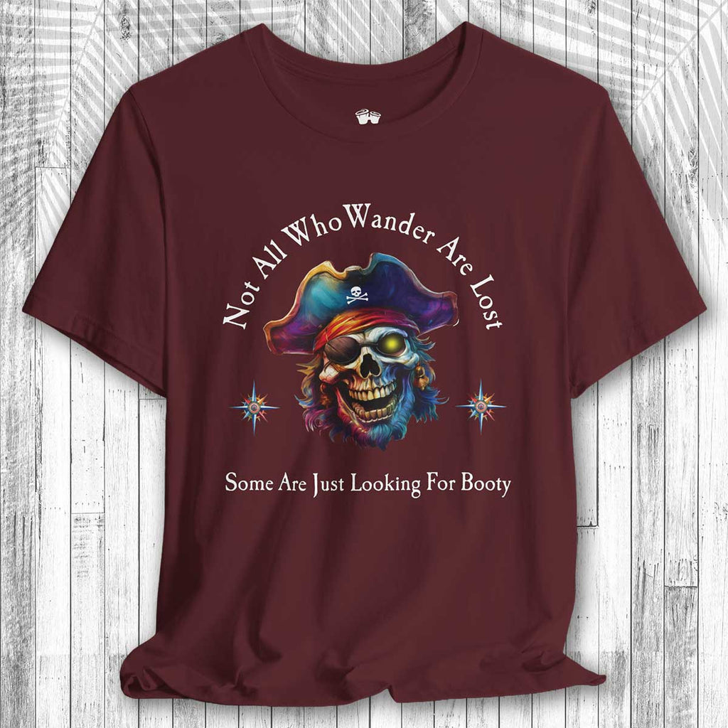 Maroon t-shirt with a colorful skull design and the text: "Not All Who Wander Are Lost – Some Are Just Looking For Booty"  on a wooden surface
