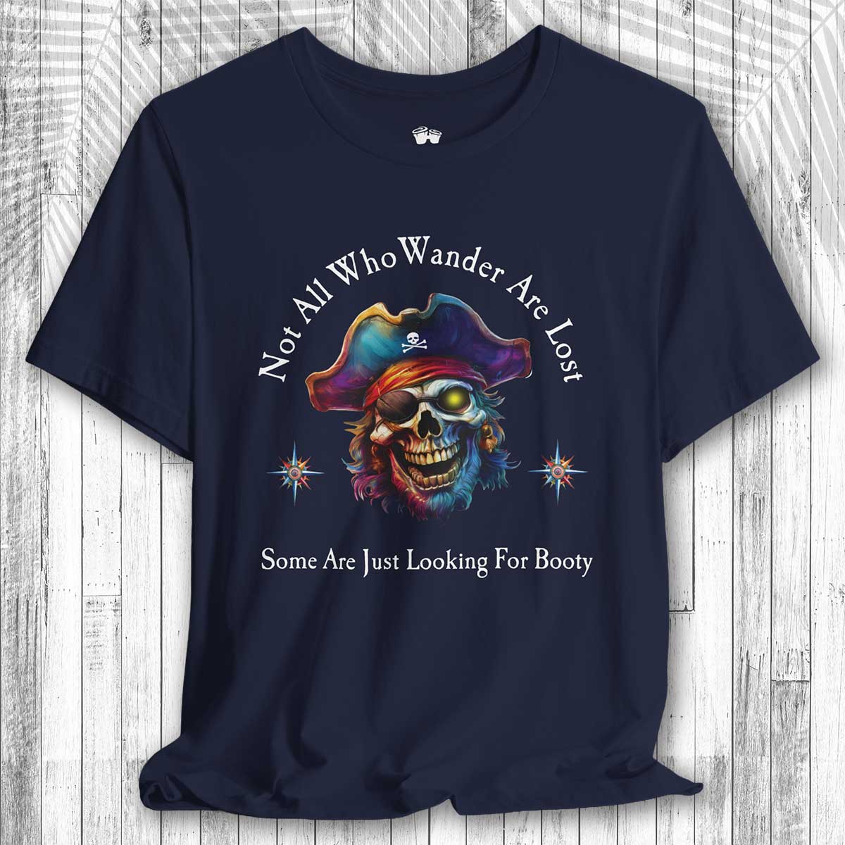 Navy blue t-shirt with a colorful skull wearing a pirate hat and the text: "Not All Who Wander Are Lost – Some Are Just Looking For Booty"  on a wooden surface