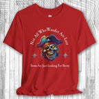 Red t-shirt with a pirate-themed design and the text: "Not All Who Wander Are Lost – Some Are Just Looking For Booty"  on a wooden surface