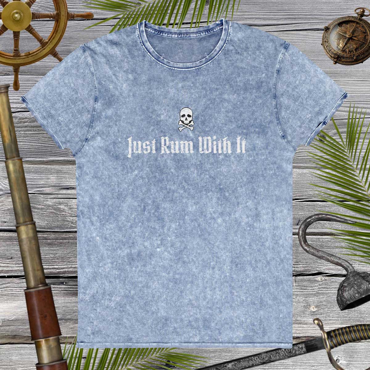 Blue t-shirt with 'Just Rum With It' text and skull design on a wooden background with nautical items.