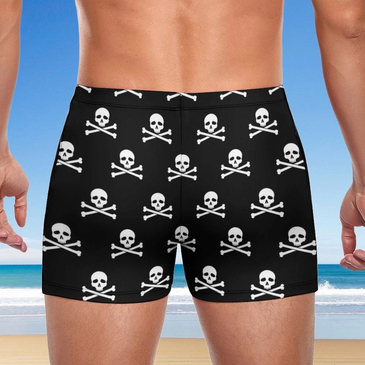 Black boxer briefs with skull and crossbones pattern worn by a person on a beach.