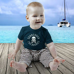 Baby wearing a shirt with a skull design sitting on a dock with a boat in the background