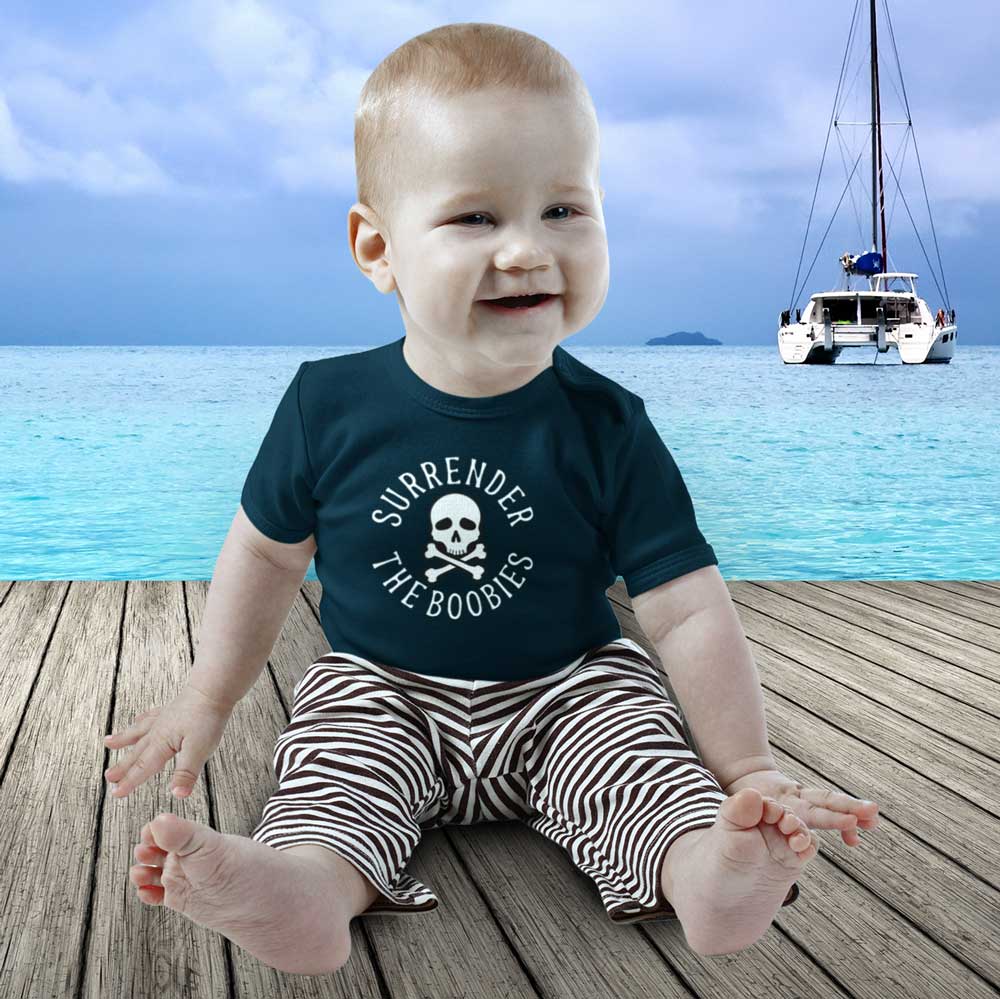Baby wearing a shirt with a skull design sitting on a dock with a boat in the background