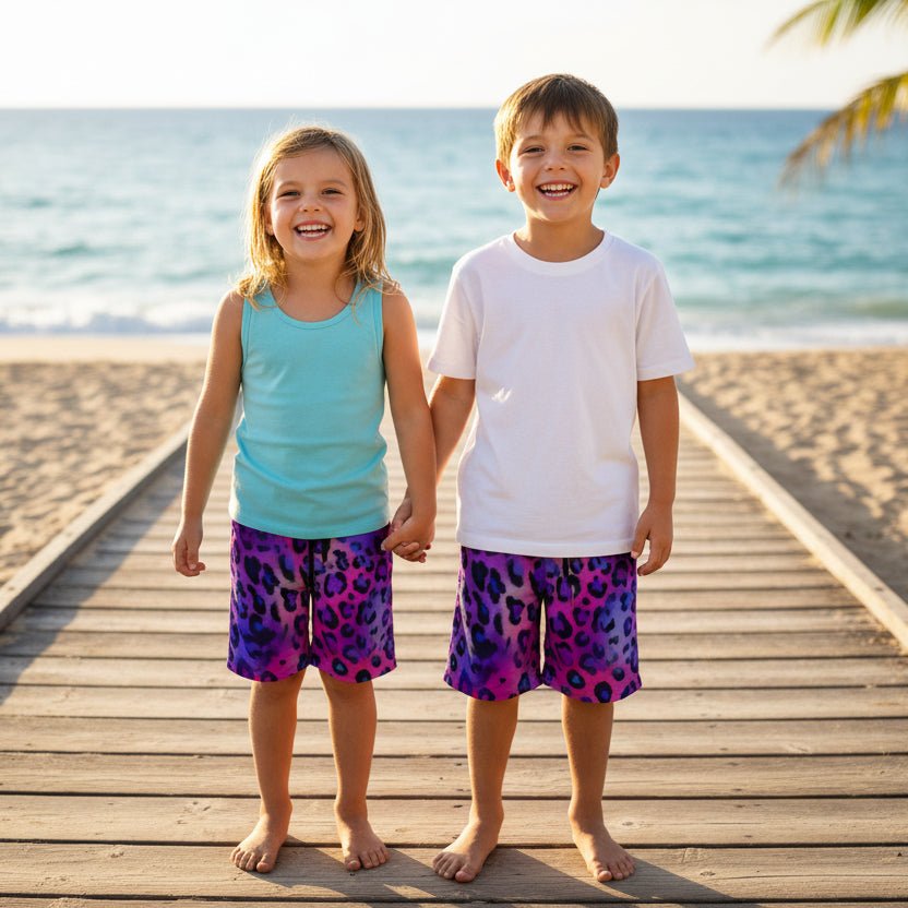 Two children standing on a wooden boardwalk by the ocean, wearing matching Kids Leopard Print Board Shorts.