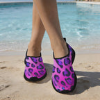 A person standing on a sandy beach poolside wearing Lightweight Running Shoes with a bright pink and purple leopard print and black trim.