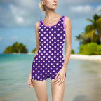 White Sand Dollars on a purple one piece vintage swimsuit in a polka dot pattern. worn by a modle standing on a beach looking for sand dollars.