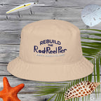 Beige bucket hat with Rebuild the Rod & Reel Pier, Anna Maria Island text on a wooden surface with fishing-related items.