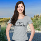 Woman wearing a gray t-shirt with text on it, standing on a beach.