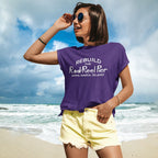 Person wearing a purple Rod N' Reel Pier t-shirt with text on a beach