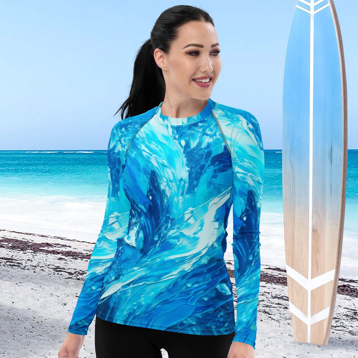 Woman wearing a blue patterned long-sleeve rash guard swimming shirt on a beach with a surfboard.