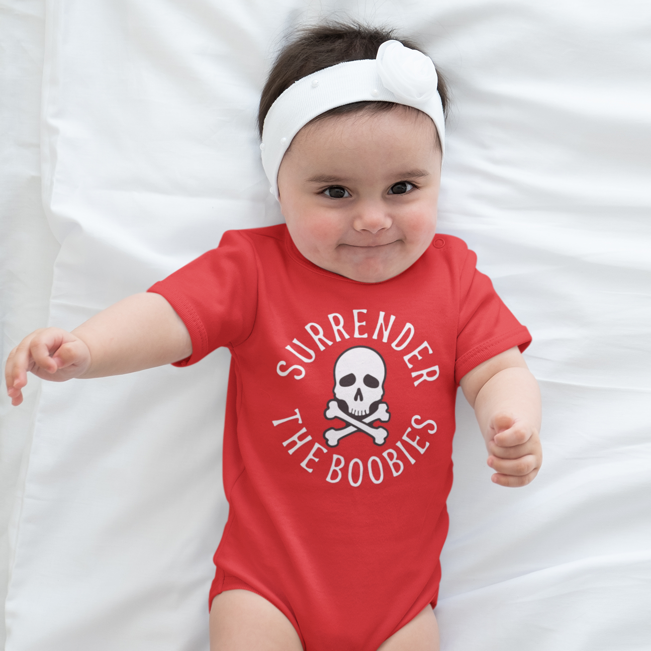 Baby wearing a red onesie with a skull and crossbones design on a white background
