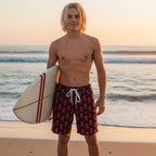 Young dude wearing black swim shorts with red skull and crossbones pattern on a white background