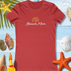Women’s Beach Mom tee in red, perfect for summer fun and beach trips, surrounded by seashells and tropical decor.