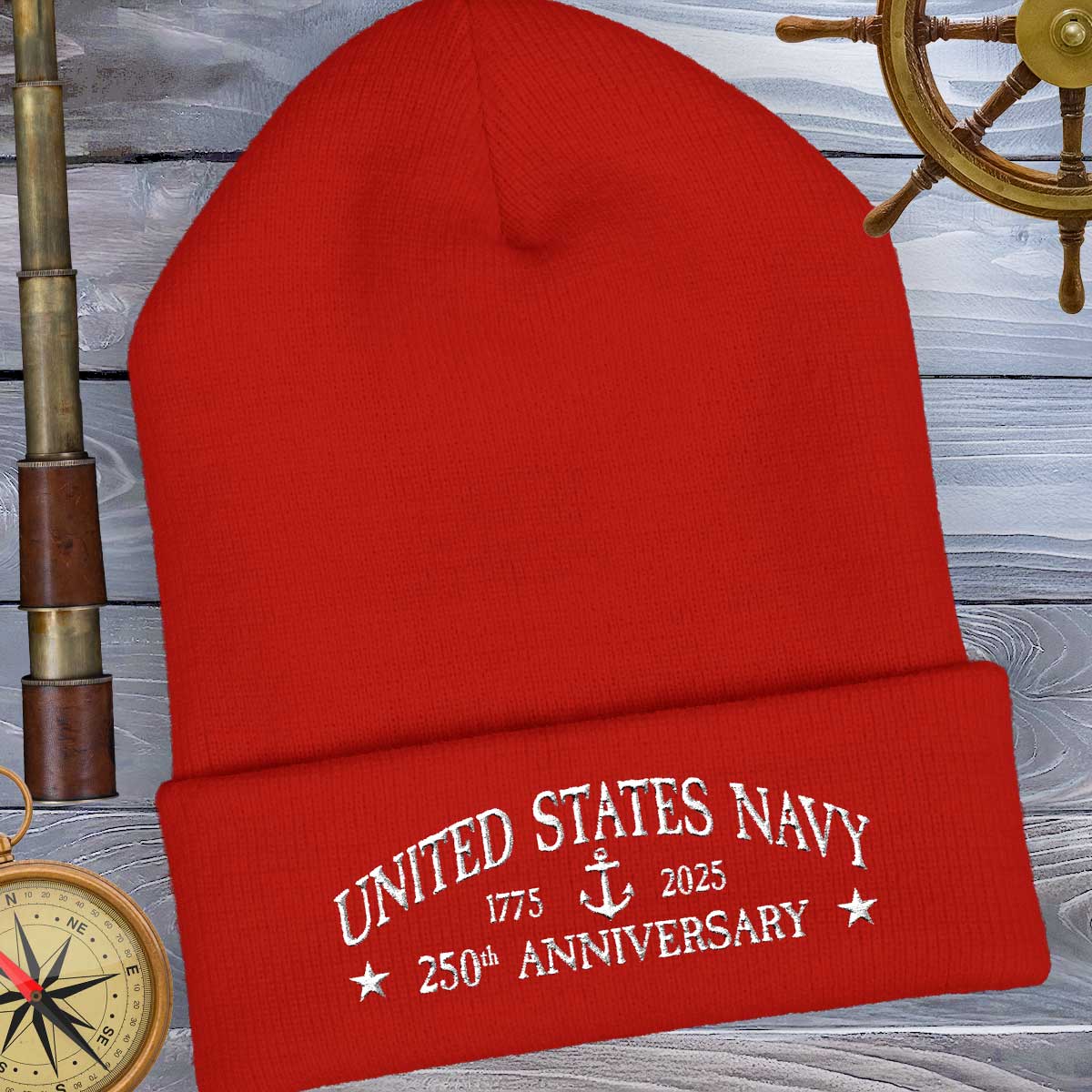 Red beanie with 'United States Navy 250th Anniversary' text on a wooden background with ship wheel and compass.