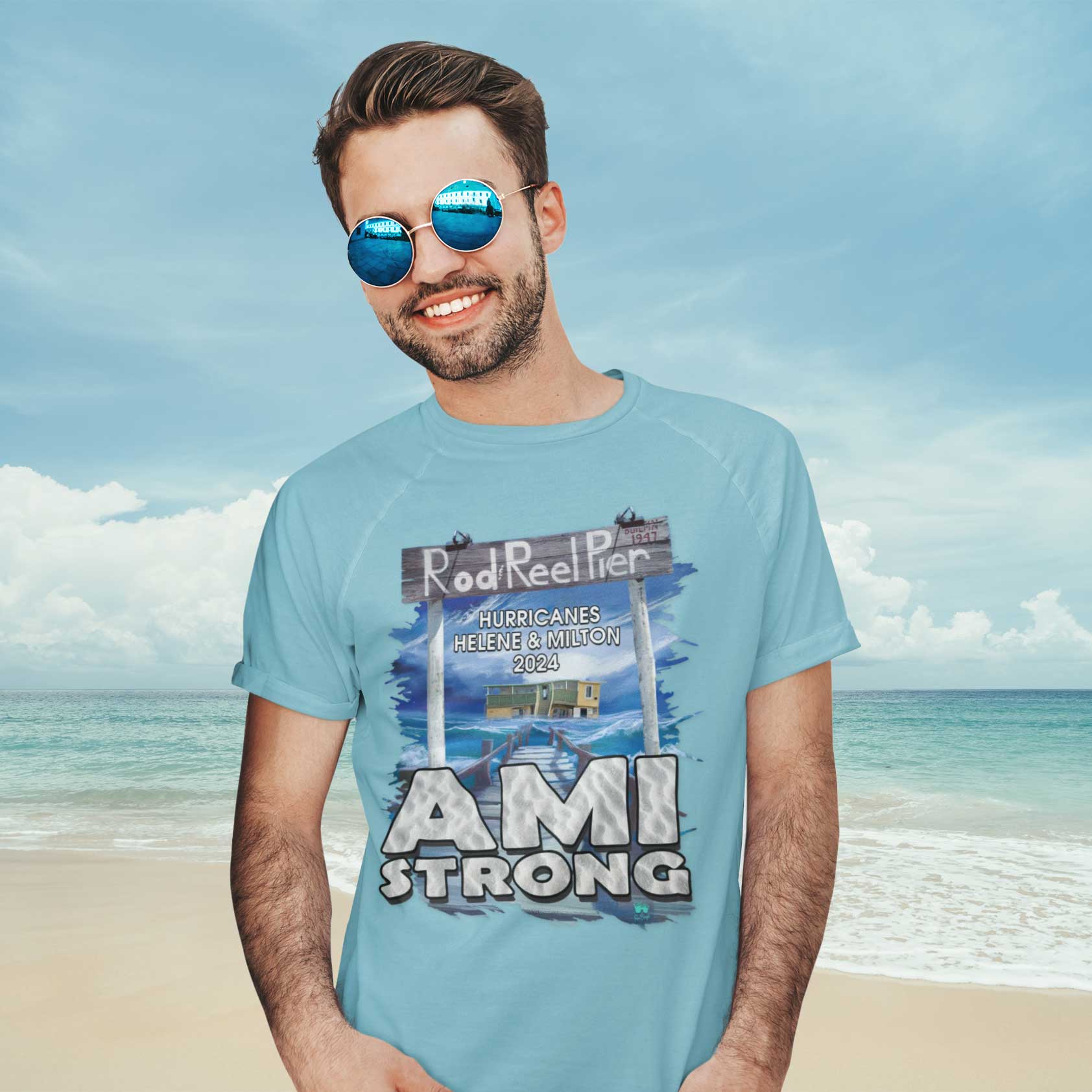 Man wearing a 'AMI Strong' t-shirt on a beach with ocean and sky in the background