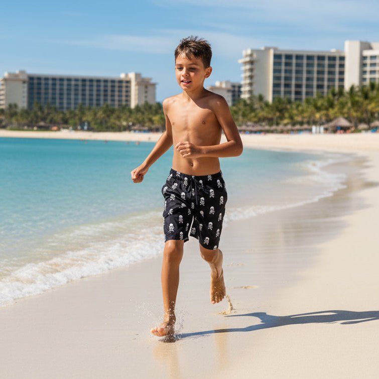 Boy running down the beach wearing Black Kids Board Shorts with white skull and crossbones pattern