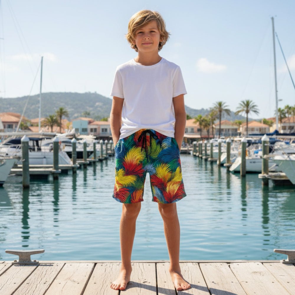Young boy wearing colorful Seagrass Pattern shorts and a white shirt standing on a dock with boats and palm trees in the background.