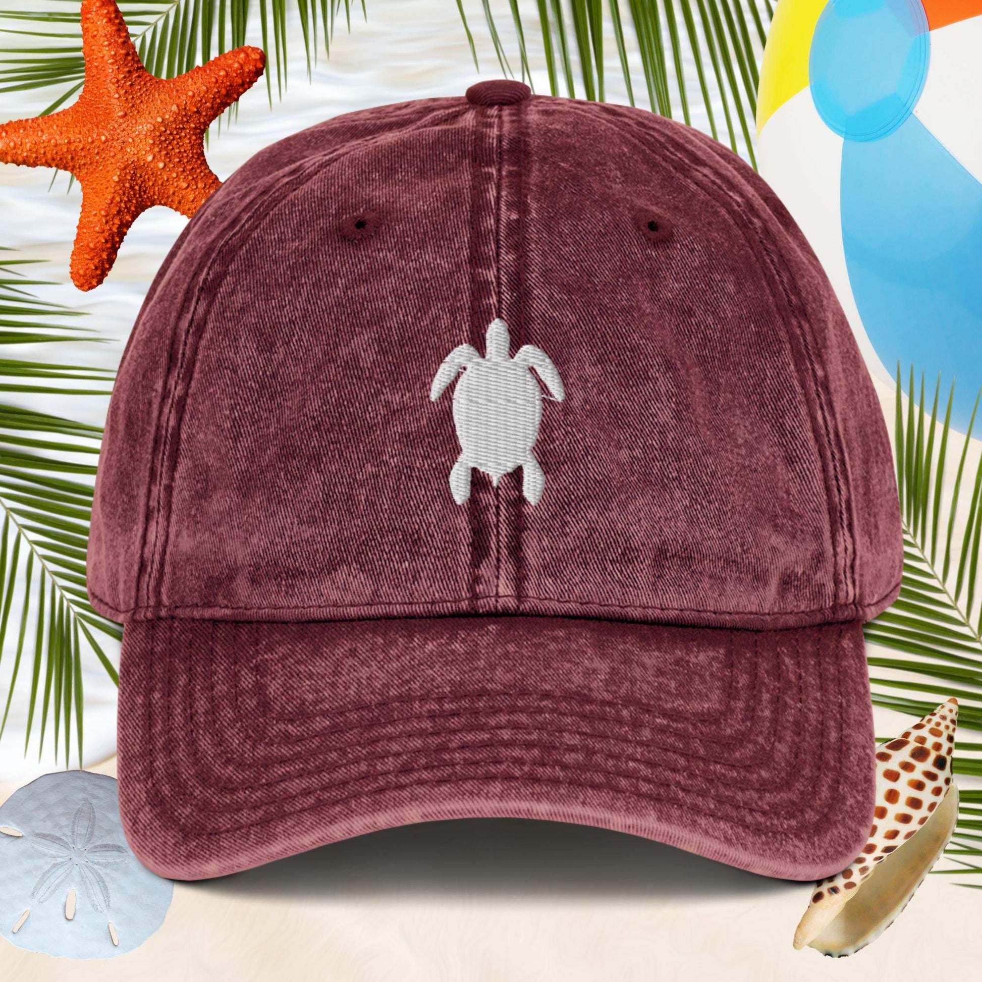 Maroon cap with turtle emblem on a beach-themed background with starfish and sand dollars.