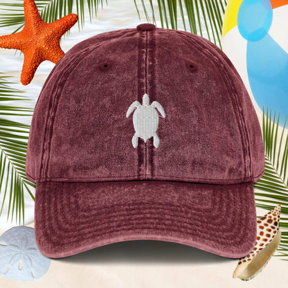 Maroon cap with turtle emblem on a beach-themed background with starfish and sand dollars.