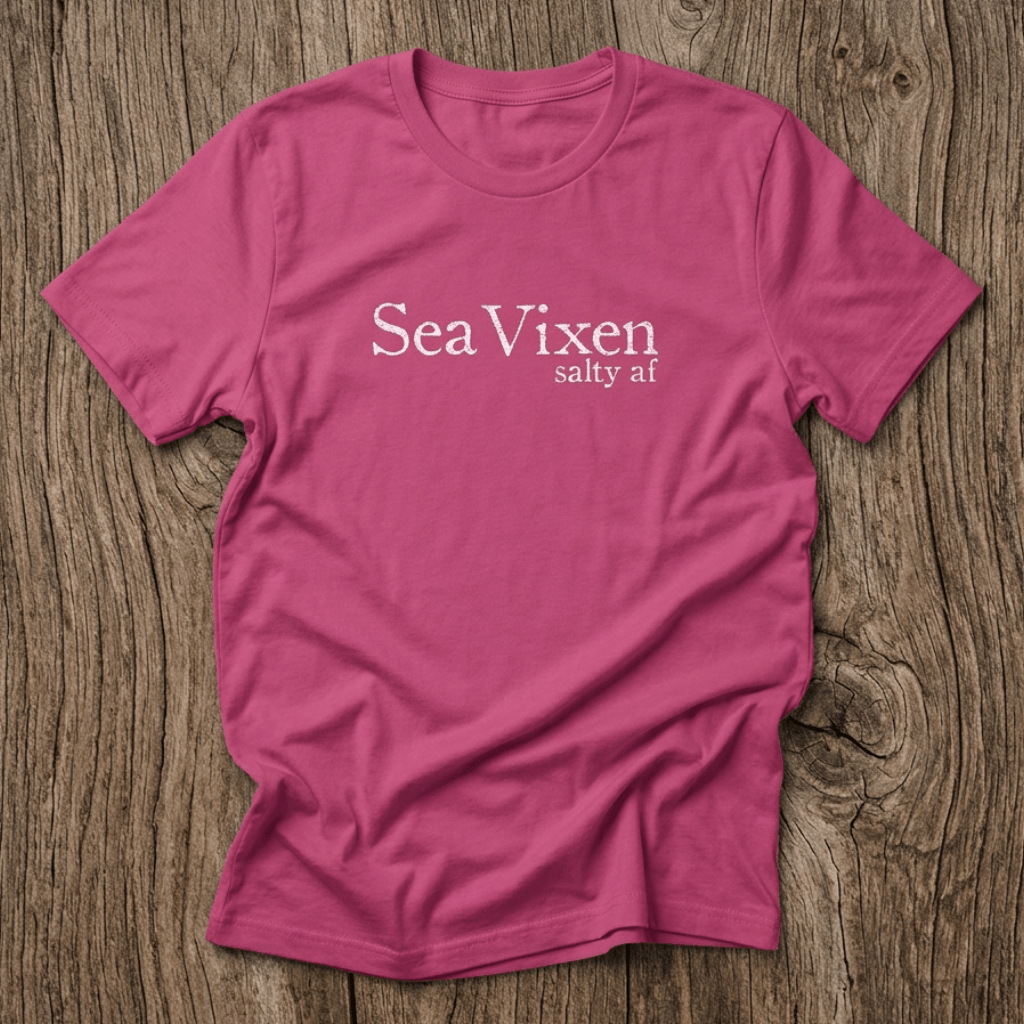 Pink t-shirt with 'Sea Vixen salty af' text on a wooden surface