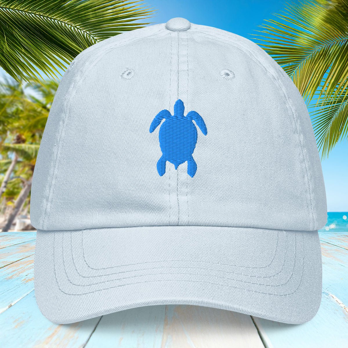 Light pastel blue cap with blue turtle emblem on a beach background