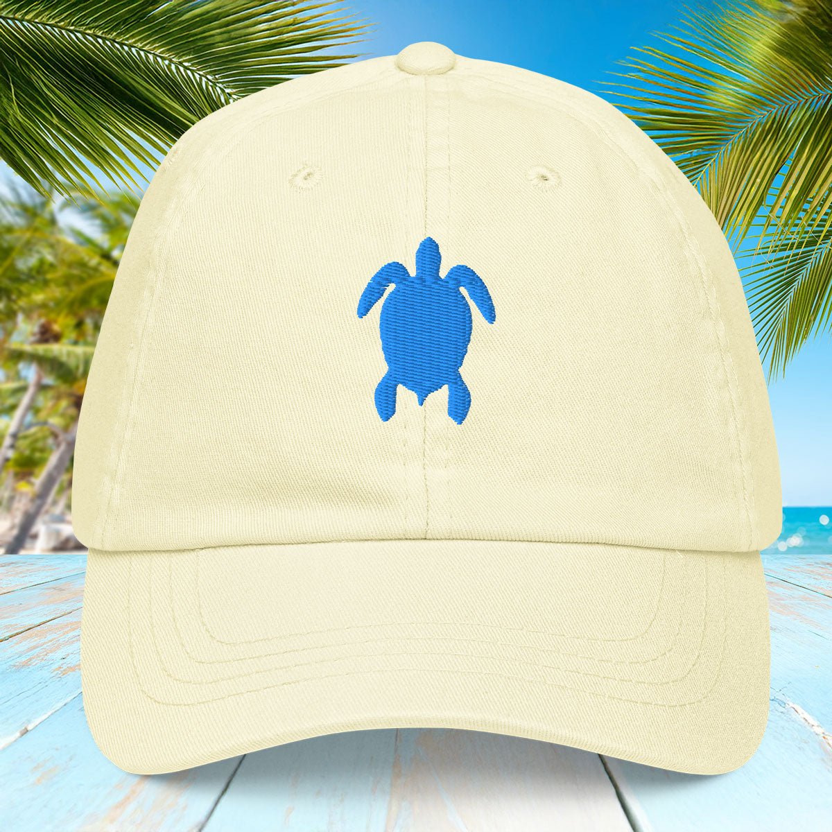 Pastel lemon yellow cap with blue turtle design on a beach background