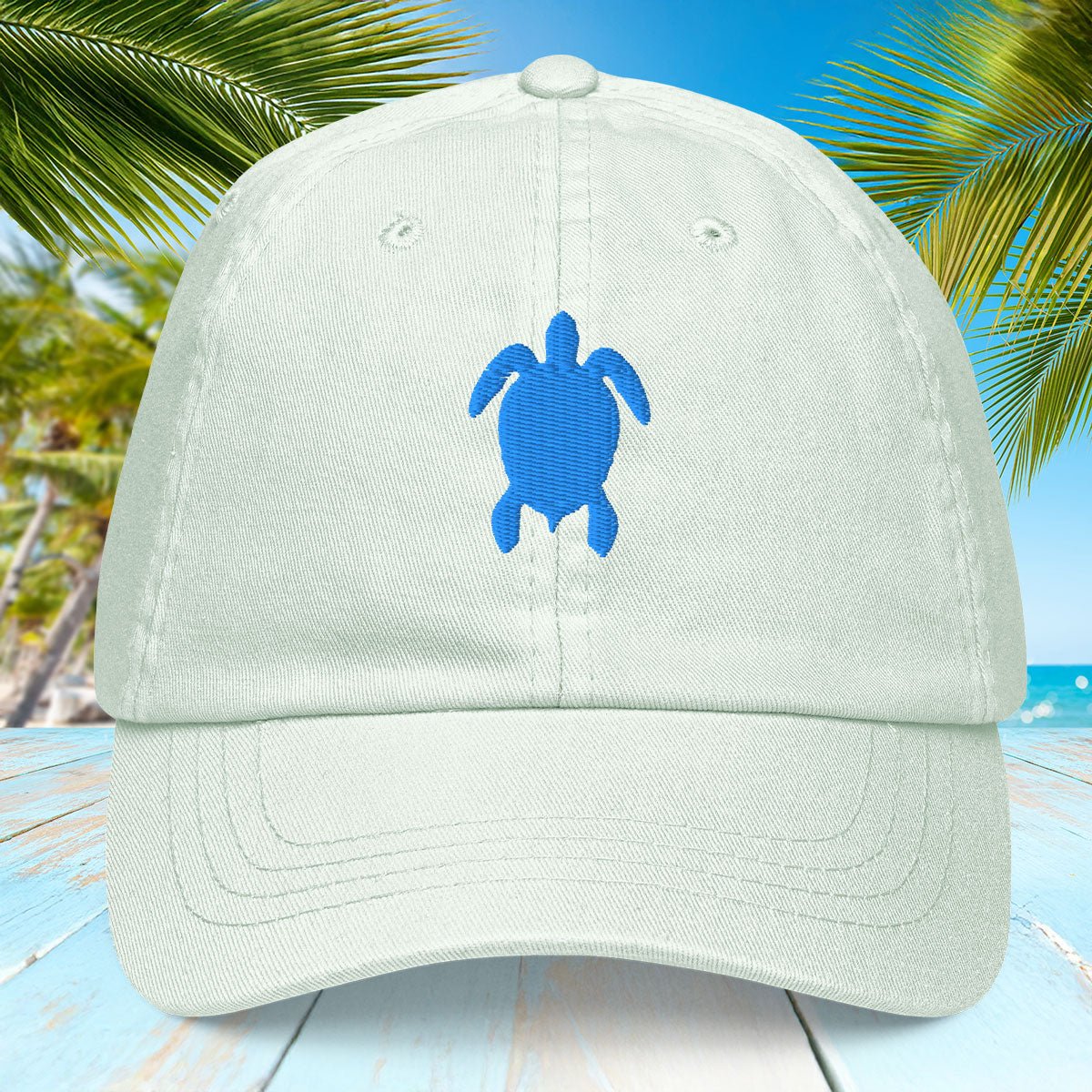 Light pastel mint cap with a blue turtle design on a beach background