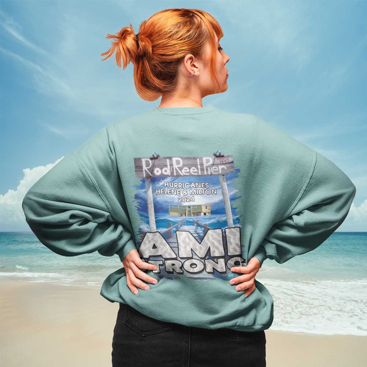 Person wearing a sweatshirt with 'Rod Reel Pier' and 'AMI TRON' text on a beach