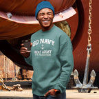 Man wearing a Seafoam sweatshirt with text, holding a coffee cup, standing in front of large ship wheels and anchors.