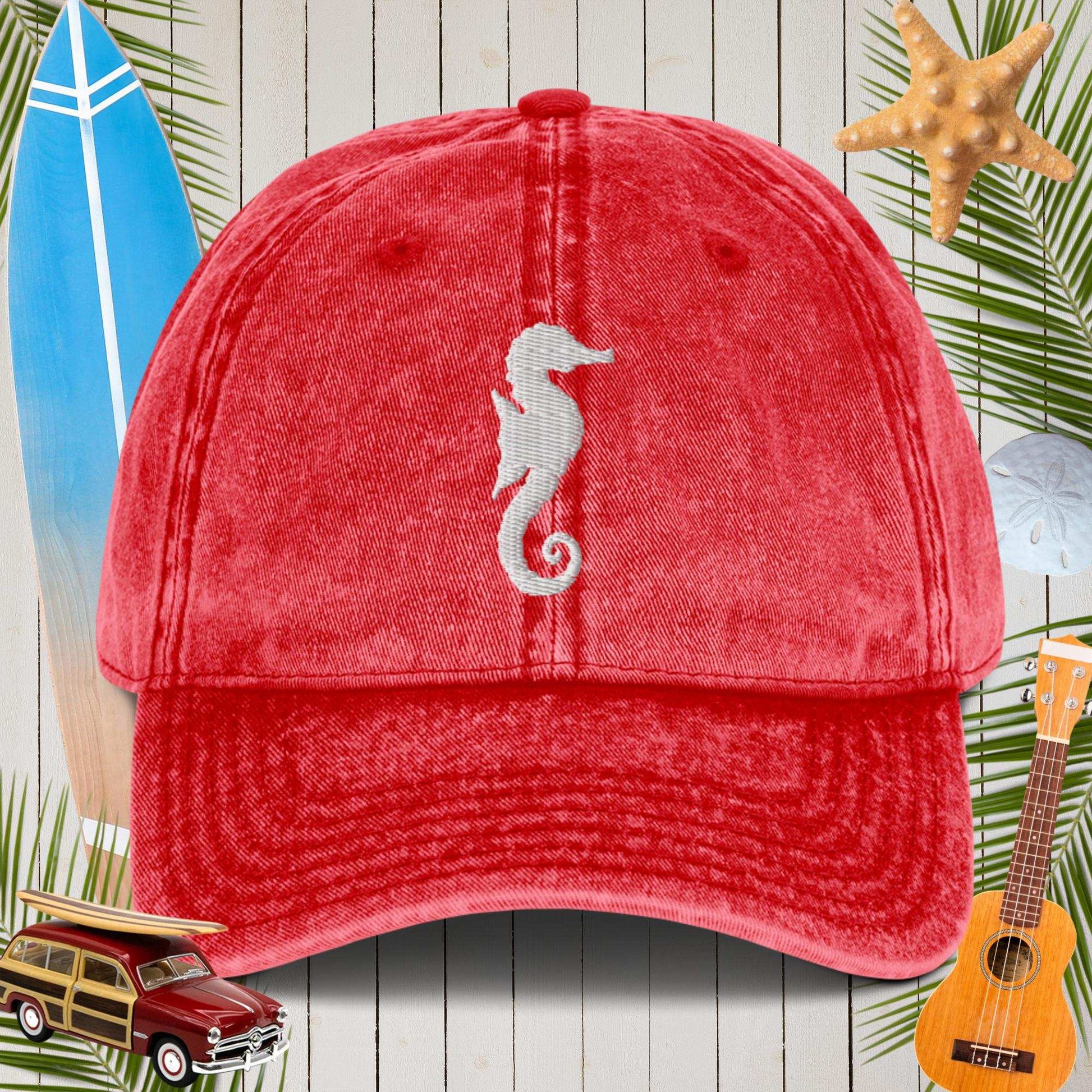 Red cap with a seahorse design on a wooden background with beach elements.