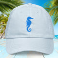 Pastel blue cap with blue embroidered seahorse design on a tropical background